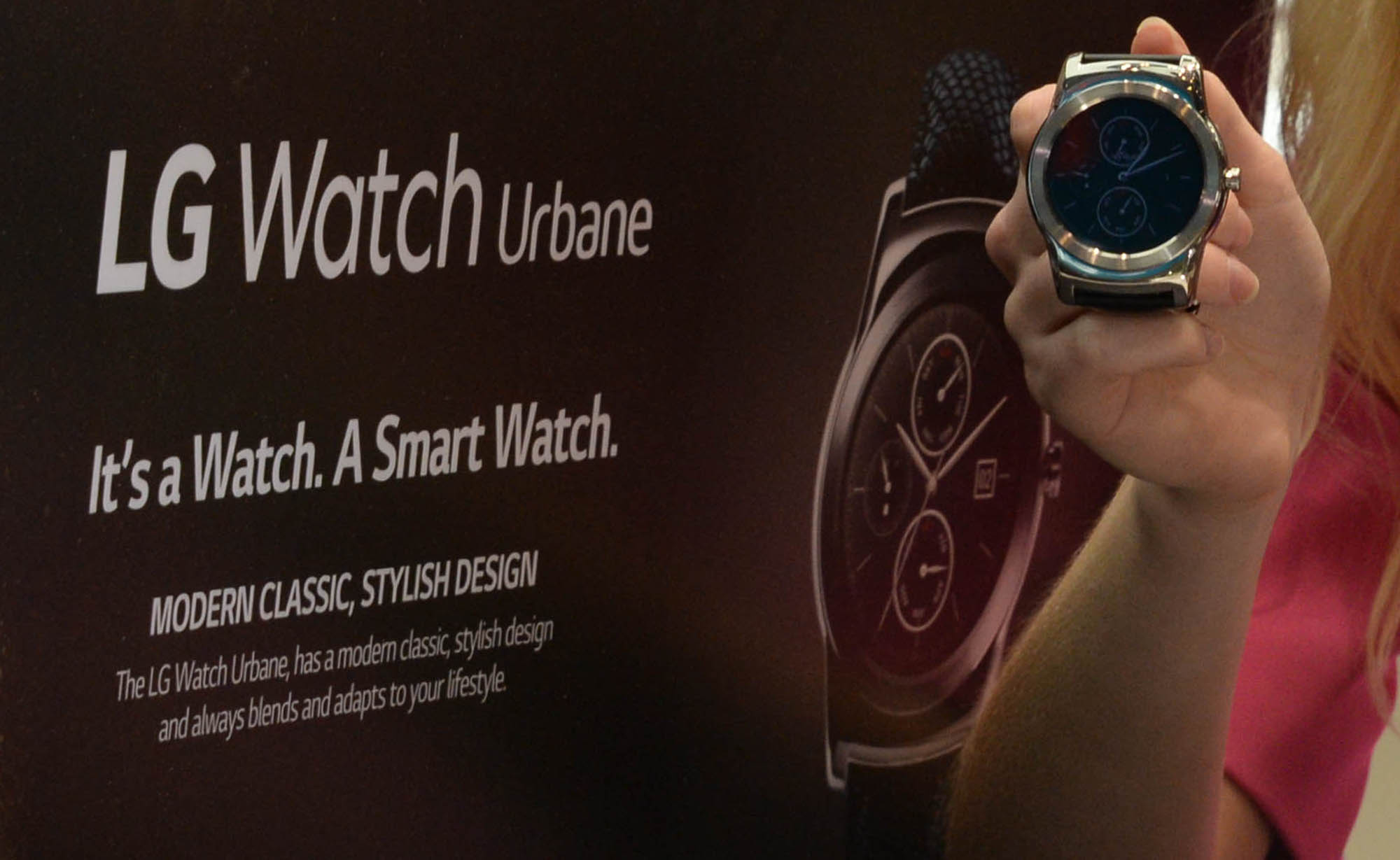 A woman holds the LG Watch Urbane in front of an large poster for the watch.